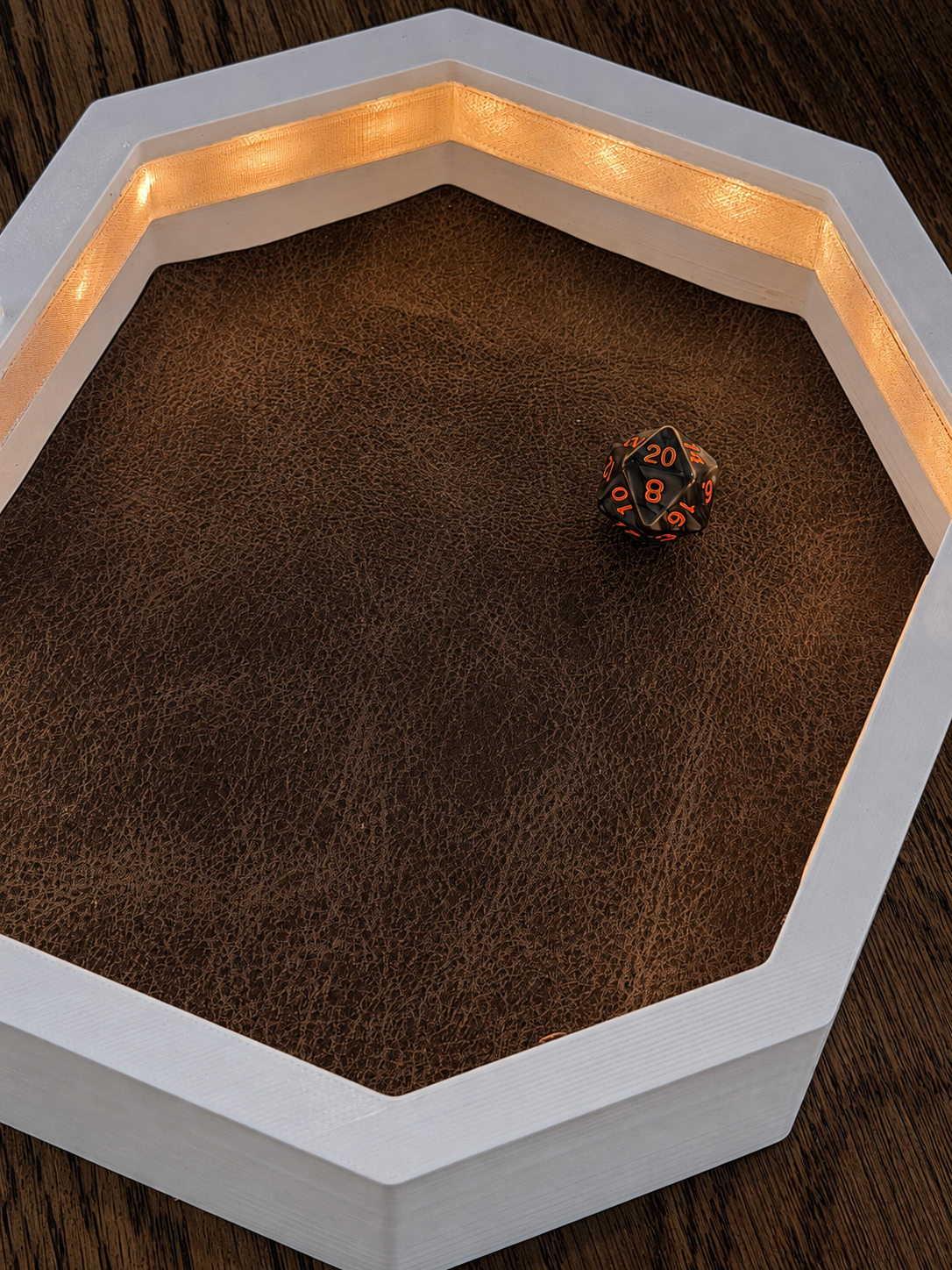 Overhead view of the white OmniRoll Origin prototype illuminated with warm LEDs and holding a physical d20